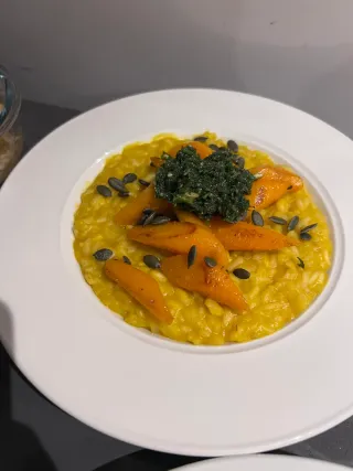 Sweet potato risotto in a wide white bowl, topped with buttered carrots, carrot top pesto and roasted pumpkin seeds