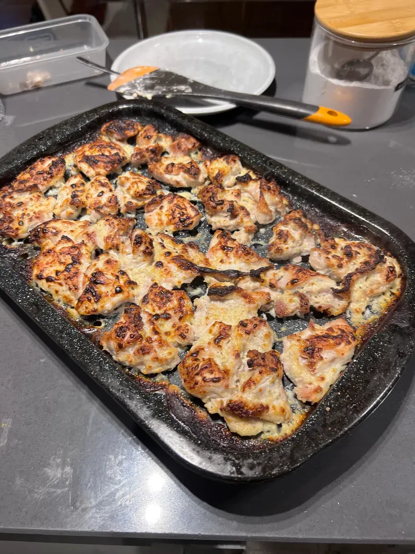 Grilled malai chicken tikka pieces, charred at the edges, on a dark roasting tray