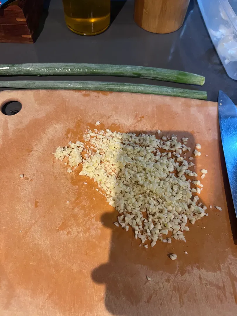 Minced garlic and two whole scallions on a chopping board