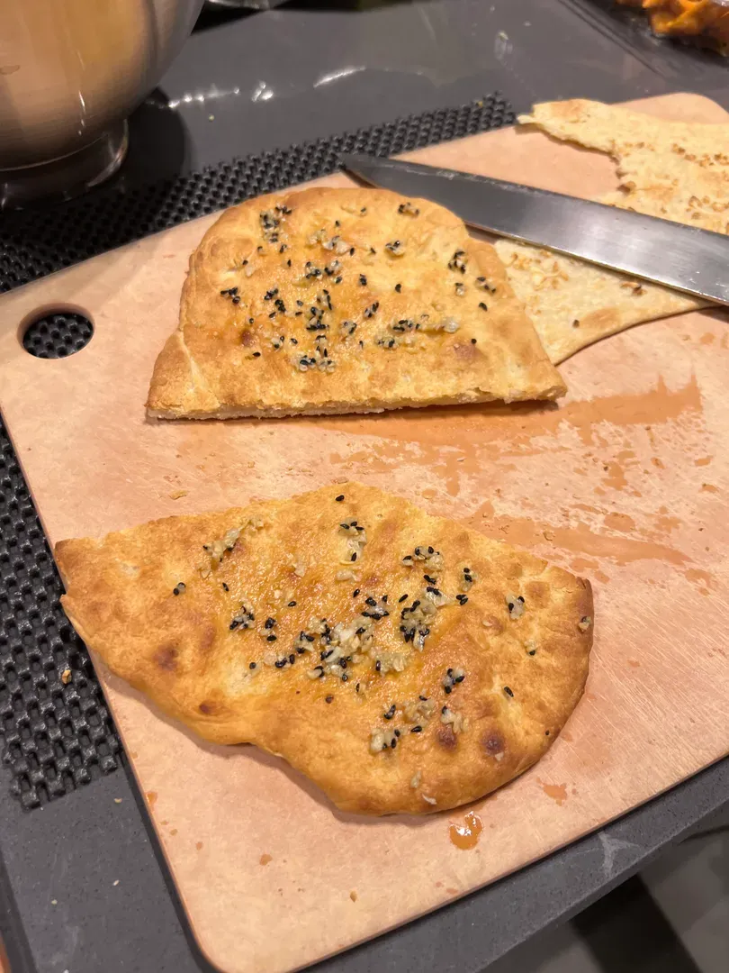 Flat, crisp-looking garlic naan topped with seeds, cut into pieces on a chopping board