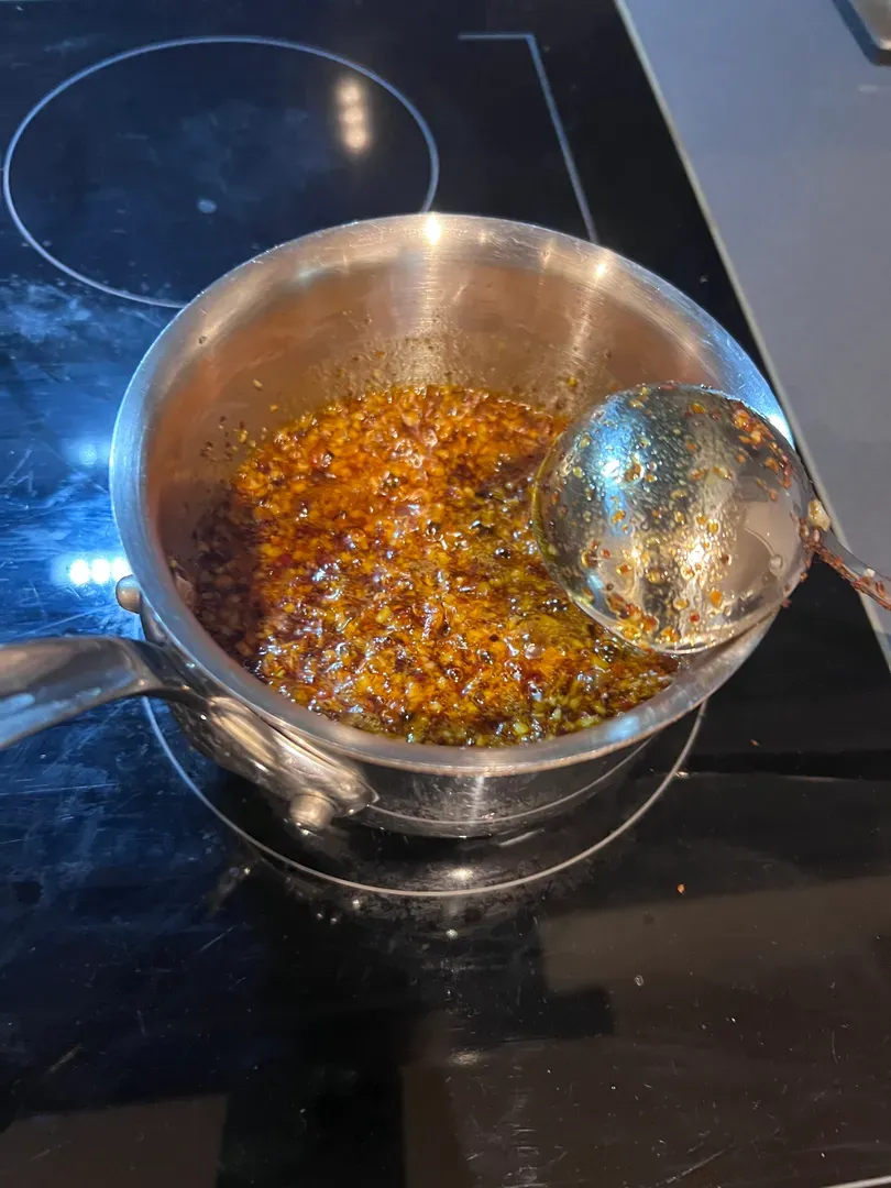 Chilli and garlic frying in oil in a small saucepan, with a ladle strainer