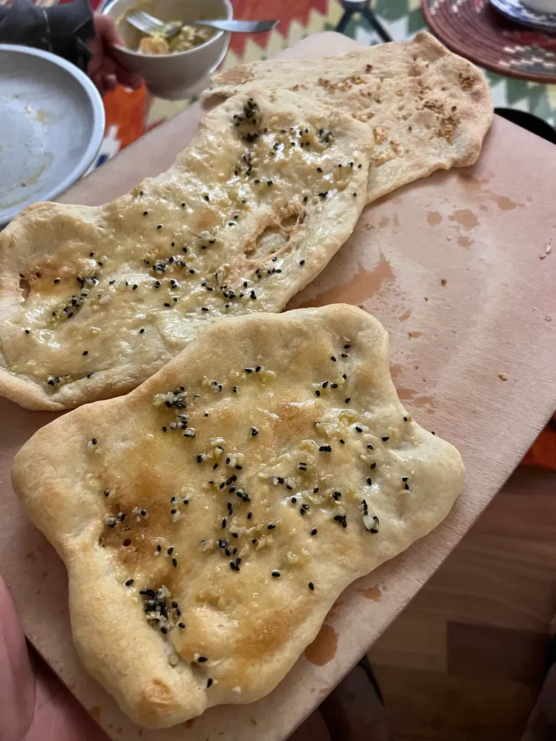 Three garlic naan with nigella seeds on a wooden board