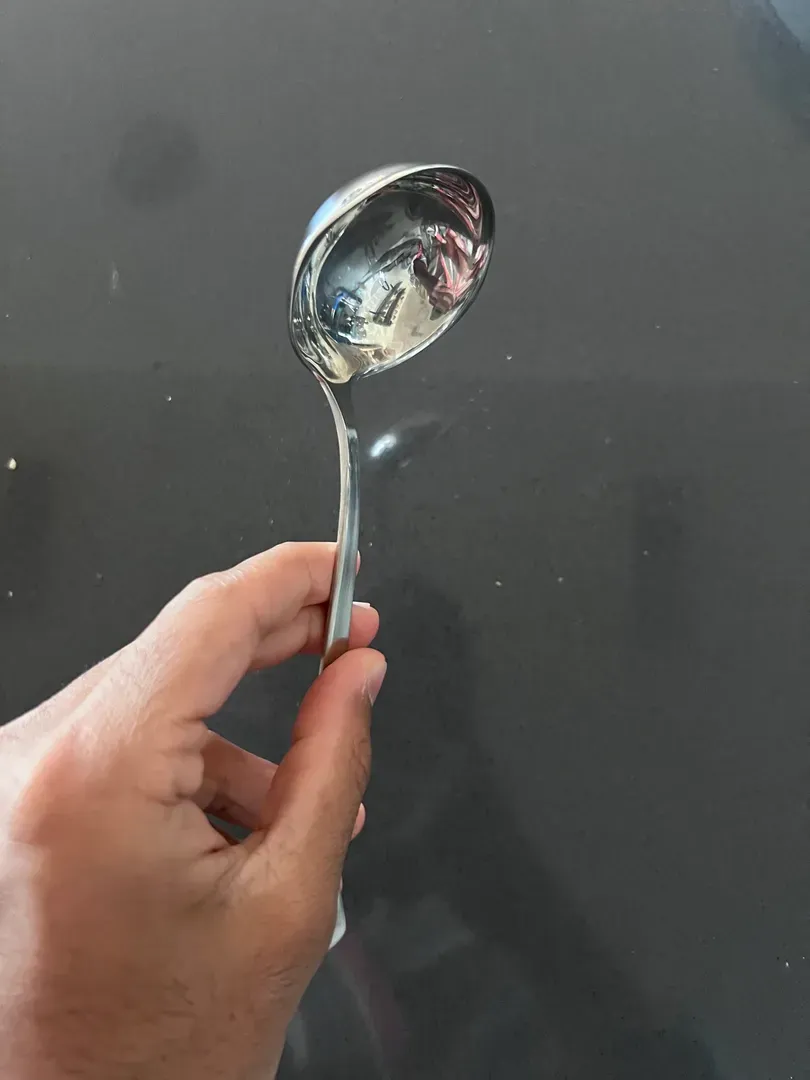 Hand holding a stainless-steel ladle with a deep round bowl