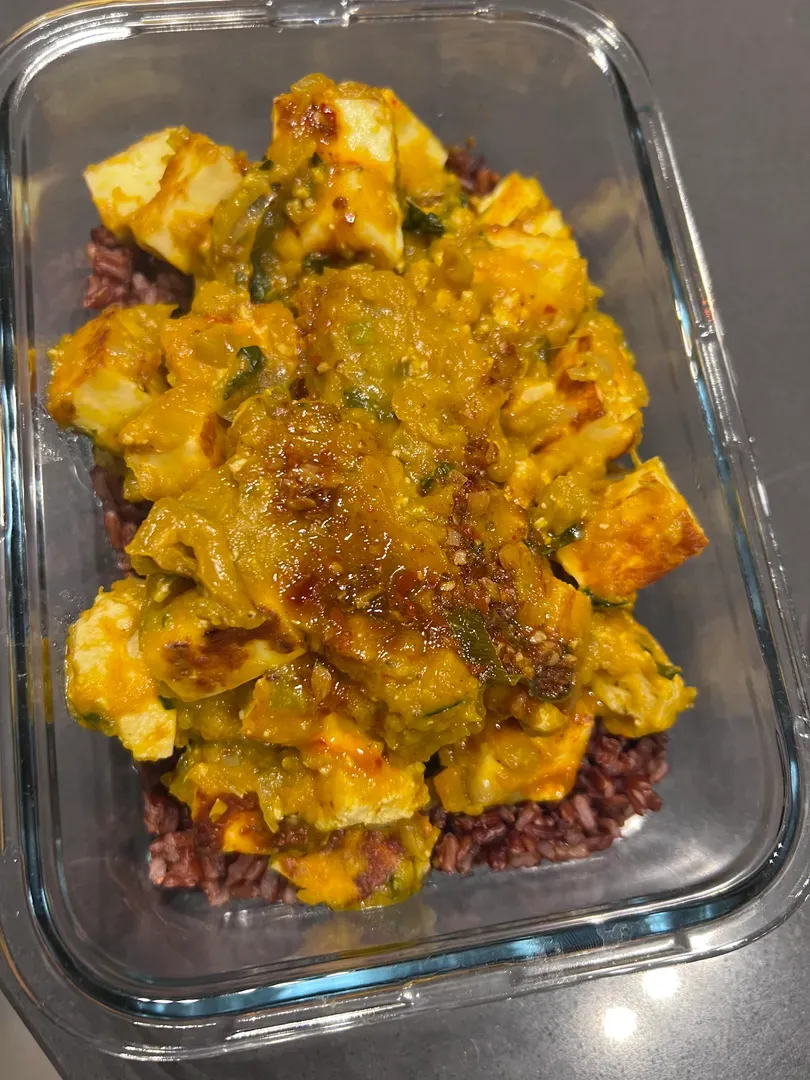 Pumpkin paneer curry over black rice in a meal-prep box, topped with the chilli oil